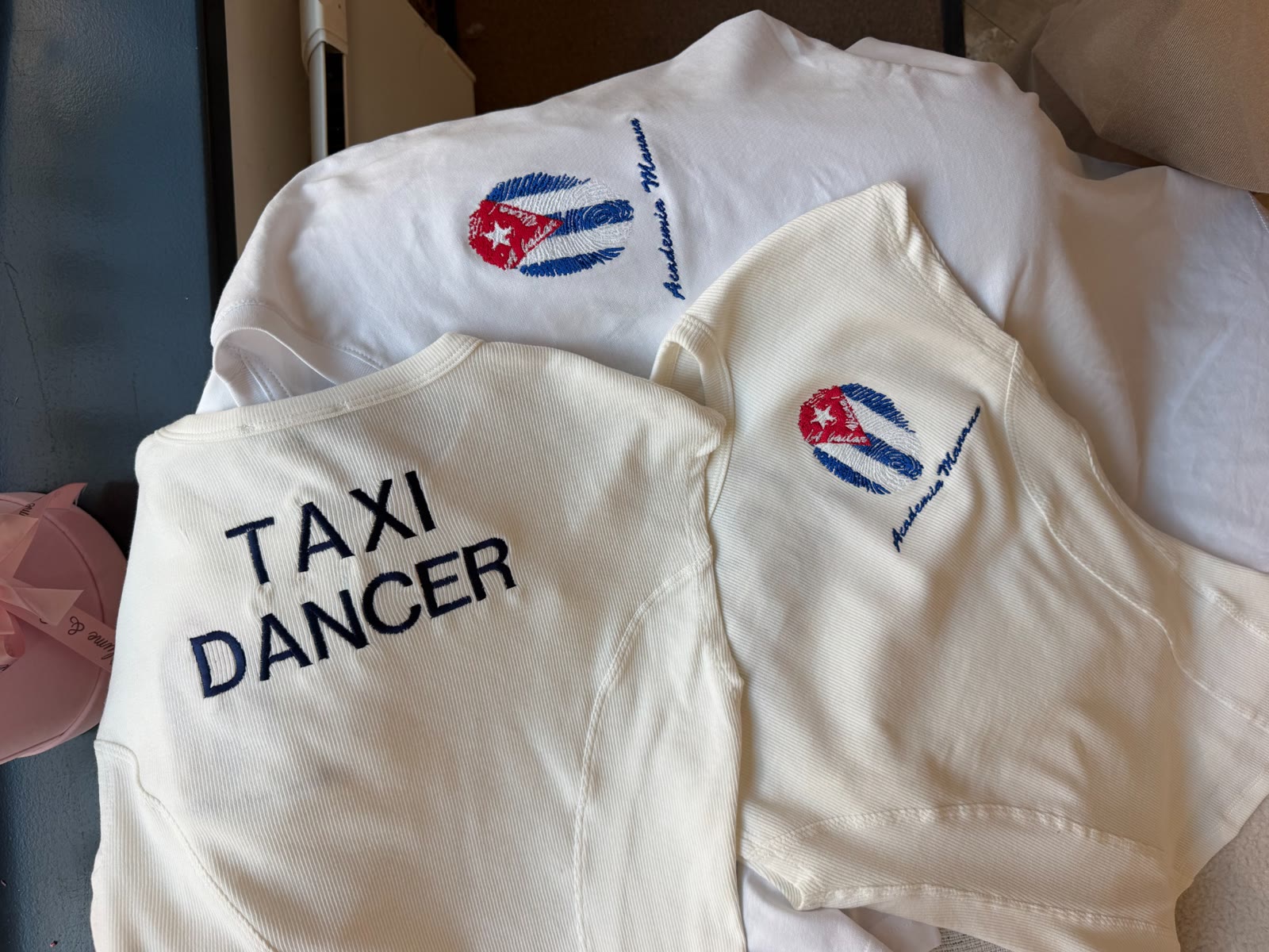 Drei weiße Kleidungsstücke mit Stickerei, darunter der Schriftzug TAXI DANCER